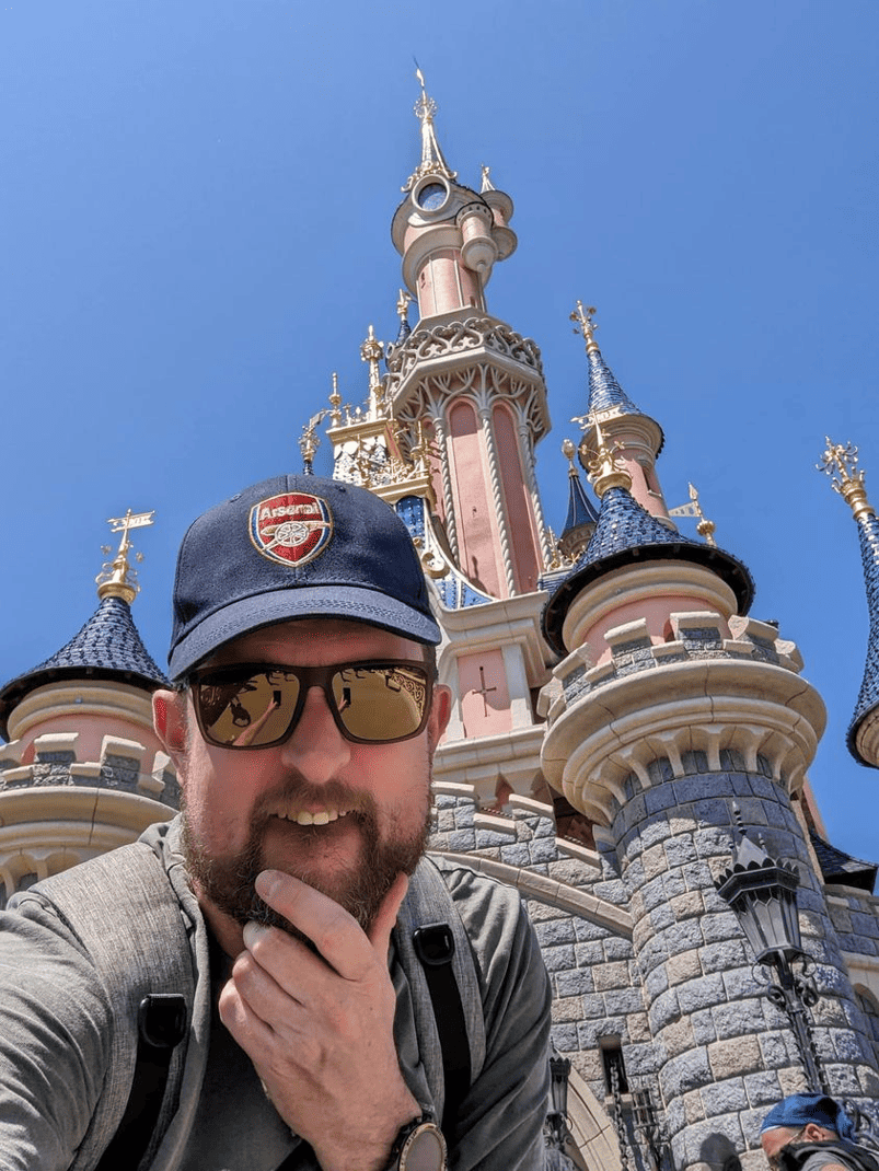 A man is taking a selfie in front of disneyland castle.