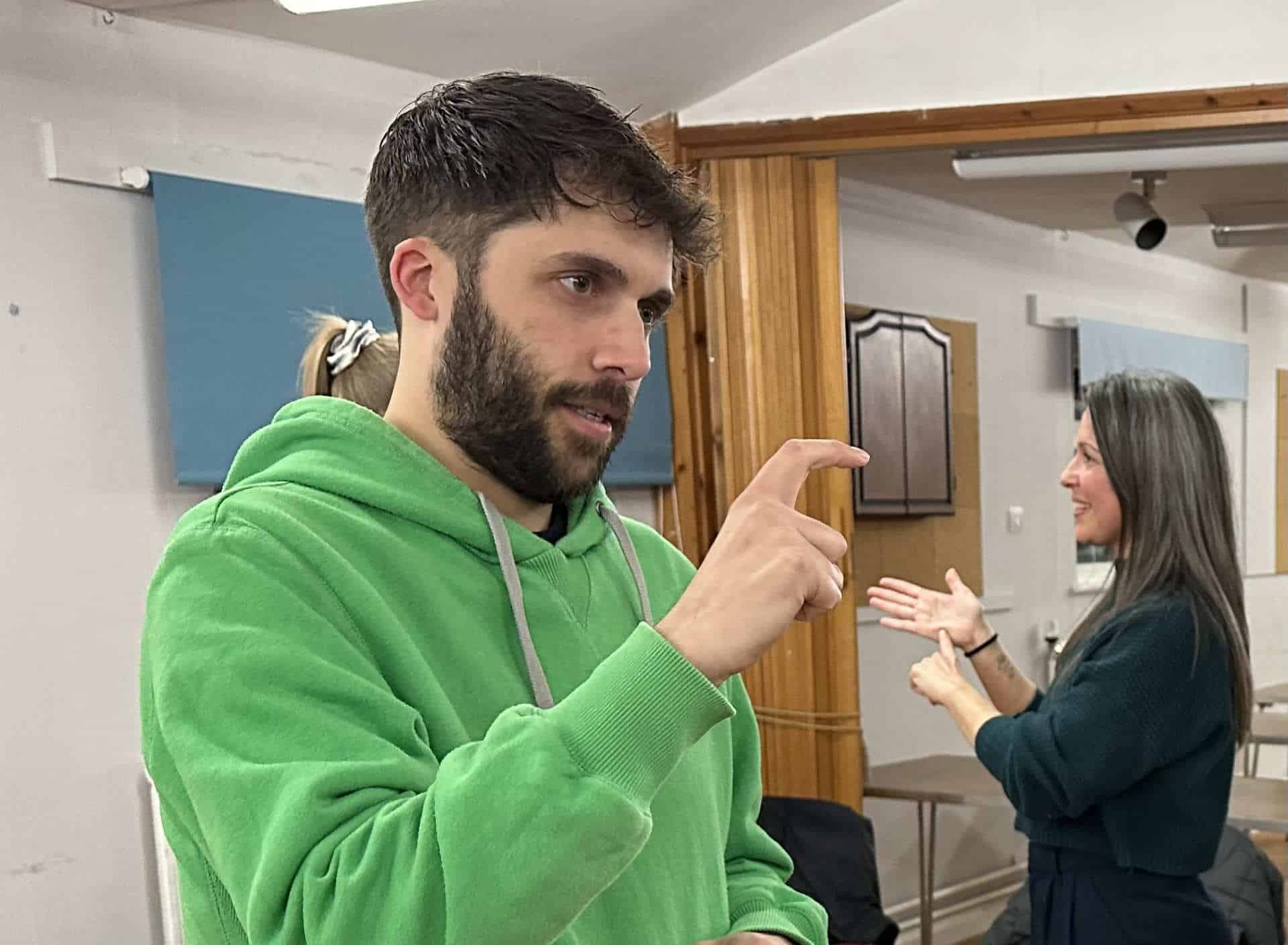 A man in a green hoodie is talking to a woman in a room.